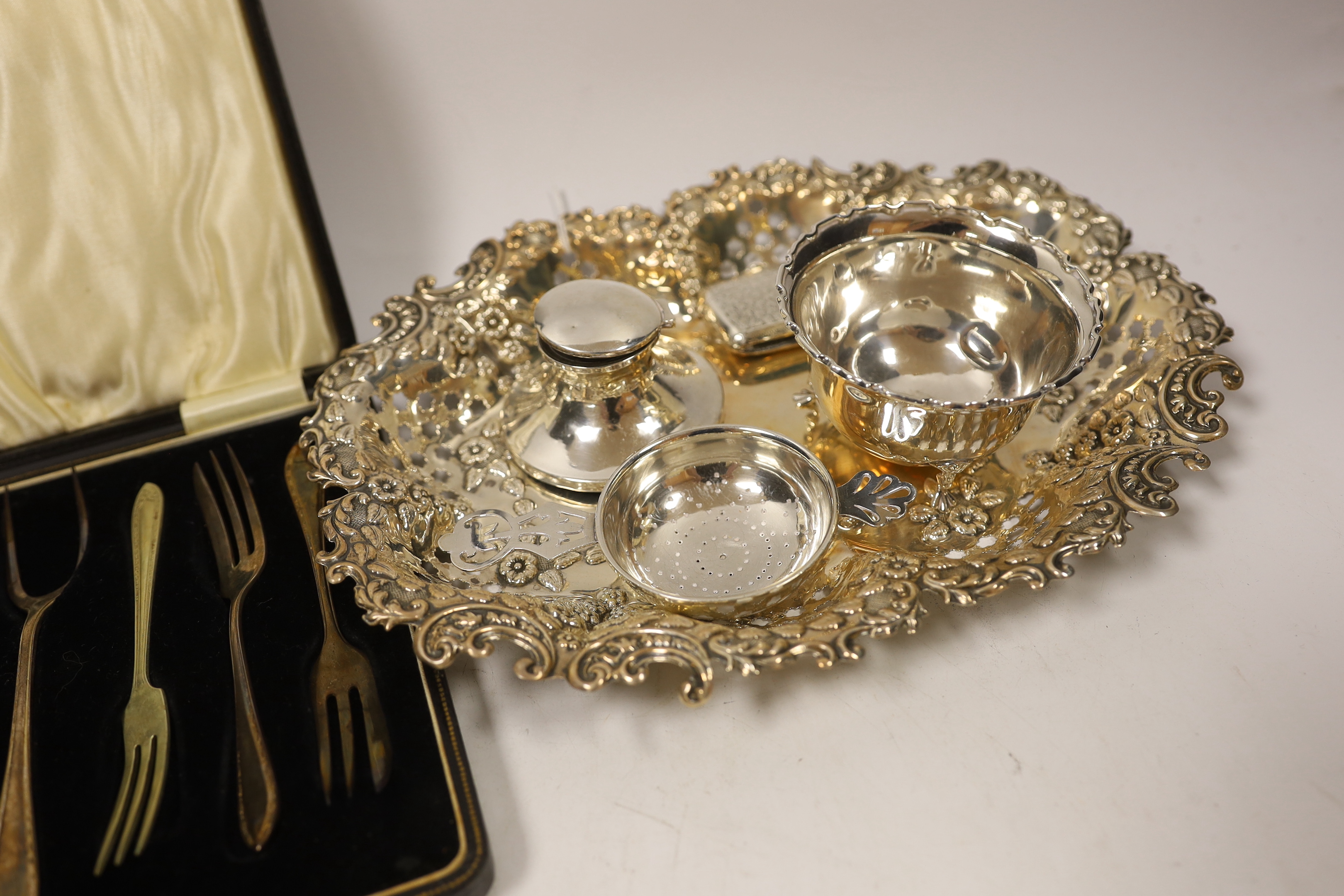 A George V pierced silver oval dish, London, 1914, 26.4cm, together with a small silver bowl, silver mounted inkstand, silver vesta case, silver tea strainer and a cased set of plated pastry forks.